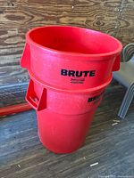 Two stacked Rubbermaid Brute branded red plastic trash cans in a wooden interior room, showing exterior condition
