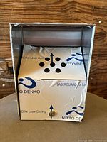 Front view of stainless steel smokers receptacle, showing ventilation holes and key-operated lock with protective skin on surface.