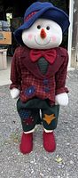 Front view of the 36 inch snowman figure dressed in a colorful patchwork outfit including a blue hat, red bow tie, maroon checked jacket with patches, patched pants, and red shoes.