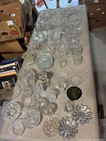 Table covered with assorted clear glassware including bowls, glasses, ashtrays, and platters in varied shapes and sizes.