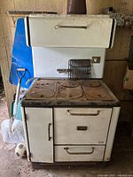 Front view of vintage Findlay enamel cookstove showing multiple burners with rust and wear, oven door, and drawer compartments below.
