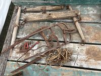 Various vintage farm tools on a weathered wooden surface including wooden yokes, hay hooks, pulley component, rope, and a small clamp