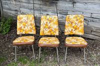 Three vintage floral chairs outdoors against wood wall, showing upholstery and metal legs.