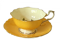 Side view of Paragon teacup on saucer highlighting yellow glaze, pedestal foot and gold trim