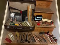 Overview of all items on staircase including open briefcase, office tools, stamps and rulers
