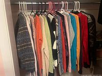 Row of assorted women’s sweaters on hangers showing variety of colors and knits