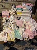 Full lot on table—mix of folded blankets, garments, hats, multiple pairs baby shoes