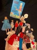 Overview of four dolls, Skooter case, pile of clothing and accessories