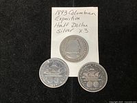 Three 1893 Columbian Exposition half dollar coins laid out on black surface showing one obverse and two reverses, with handwritten note confirming identification and quantity.