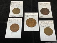 Five coins laid out with paper holders and handwritten notes describing each coin.