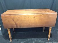 Full side view of antique wooden drop leaf table closed, showing straight edges and smooth refinished top.