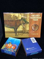 Photo showing the sealed gold plated Benjamin coin pack with holograph featuring the Last Tasmanian Tiger, alongside two boxes of Australian Sea Life The Reef silver proof coins from Perth Mint.