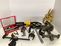 Wide view showing full set of automotive tools including clamps, flaring tools, chain wrench, and open-end wrenches arranged on a white surface.