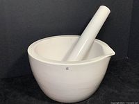 Extra large white porcelain mortar and pestle set with pestle resting inside the mortar. Mortar has a spout and smooth glaze exterior, unglazed interior, some marks visible.
