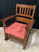 Full view of Craftsman style oak rocker with red/pink tufted cushion on seat showing chair design and wood finish.