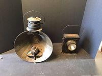 Two lanterns shown side by side on a flat surface against a dark background, showing relative sizes and shapes.