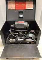 Open metal case showing tool post grinder, motor, quill attachments and abrasive wheels