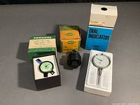 Overall view of three items: Federal dial indicator, no brand dial indicator, and Greenlee radio chassis punch with original boxes.