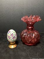 Fenton hand painted glass egg and cranberry glass vase shown together on black background.