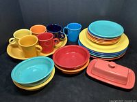 Full set arranged showing dinner plates, salad plates, cereal bowls, mugs, butter dish, and platter in multiple bright colors