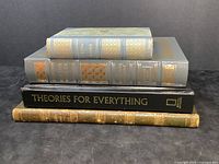 Stack of four books showing varied binding styles and titles including 'Theories for Everything' and 'Geditche'