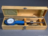 Fowler dial bore gauge inside open wooden box showing the gauge and compartmentalized storage area.
