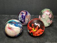 Four glass paperweights arranged together showing colors and designs: red, white and blue swirl; pink flower with blue swirl; pink flowers and bubbles; butterflies and flower.