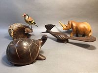 Four handcrafted wooden animal sculptures in a group display: chickadee on petrified wood, roadrunner, turtle, and rhino.