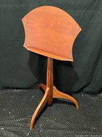 Front view of the wooden music stand showing the curved music rack and tripod base.