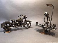 Two Hinz & Kunst welded metal sculptures: a motorcycle and a patient figure on an examination table with lamp