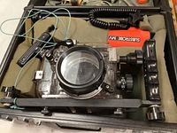 Clear plastic Ikelite underwater camera housing with black lens port and red Substrobe MV unit attached with coiled wire, sitting in padded carrying case.