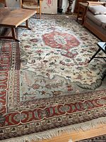 Full view of large wool area rug showing central medallion, geometric floral patterns and fringe edges under furniture in living room.
