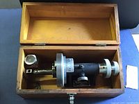 Angle dresser measuring tool inside the wooden case showing the tool with a drill bit on the spindle.