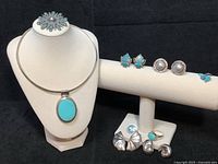 Group display on black cloth: necklace bust with sunburst brooch, collar with pendant; cufflinks and earrings on bar; clip-ons, mismatched studs and ring on block.