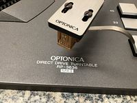 Close-up of tonearm headshell showing cartridge and Optonica branding on plinth