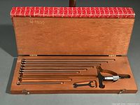 Opened wooden box containing the set of stainless steel extension rods, micrometer depth gauge, and wrench neatly arranged in fitted slots.