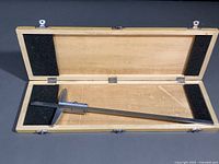 Open wooden box containing the stainless steel vernier depth gauge positioned inside, showing the full box dimensions and padding.