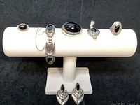 Full set of six sterling silver and onyx jewelry pieces displayed on a jewelry stand, including a pair of clip earrings, two rings, two pendants, and a link bracelet.