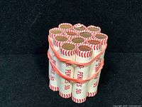 Top view of 12 tightly bundled unopened bank rolls of pennies wrapped in white and red paper.