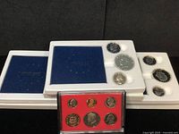Four proof sets displayed: three white Bicentennial silver proof sets with blue inner cases and one 1982 proof set with red interior and plastic casing.