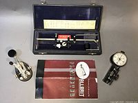 Photo showing all three items: Rucker Co. planimeter in blue case with booklet, Speed-X Morse key, and Abney level with compass.