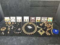 Full assortment of vintage costume jewelry laid out on black background. Includes earrings on cards from Anne Klein, Liz Claiborne, Adrienne Vittadini, necklaces, brooches, and other pieces.