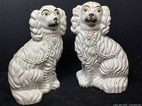 Front view of pair of white ceramic Staffordshire dog statues showing hand painted faces and pink collars.
