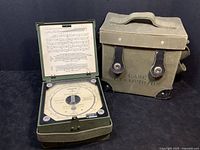 Full view of the open barometer inside its hinged case alongside the closed military carrying case in olive green fabric.