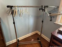 Front and side views of an adjustable chrome garment rack with an assortment of plastic, metal, and wooden hangers hanging on the crossbar. Rack has black caster wheels and adjustment clamps on vertical poles.