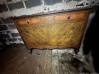 Front view of antique wooden dresser showing curved drawer fronts with carved heart motif on top drawer, scrollwork on lower drawers, turned legs and vintage hardware