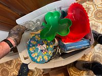 Top view photo of box showing colorful plastic shamrock and heart trays, ceramic Easter-themed plate, glass pie dish and box with assorted kitchen items.