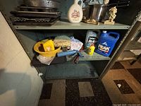 Lower angle of metal shelving unit showing automotive fluids, cleaning supplies, and parts of kitchenware and figurines.