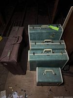 Photo showing 4-piece green hard-sided luggage set with cream trim and brass-tone hardware alongside a maroon leatherette suitcase
