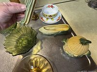 Green and amber pressed glass bowls, ceramic corn dishes including one with lid, and a children's bowl and plate set with tiger and flowers on a countertop.